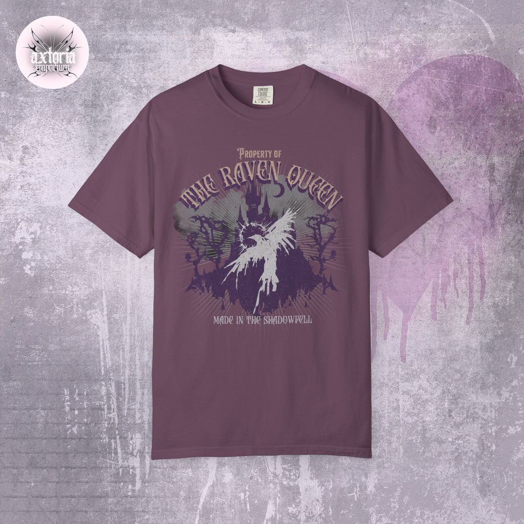 Purple-maroon Dungeons and Dragons t-shirt with 'Property of the Raven Queen Made in the Shadowfell' design on a textured gray background.